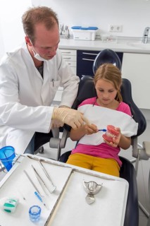 Dentist showing a girl the proper use of a toothbrush