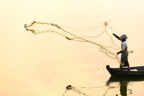 Fisherman in a boat tossing out a net