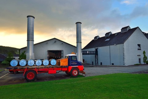 Old lorry loaded with whiskey barrels parked in front of a distillery