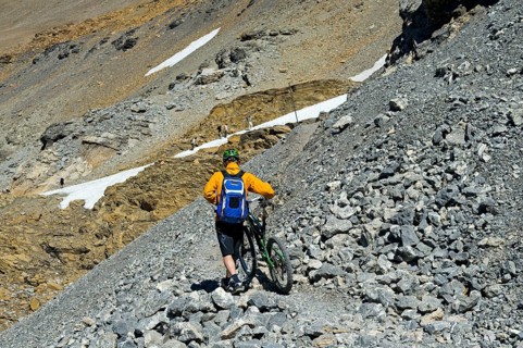 Mountain biker pushing his bike on a single trail in rocky terrain