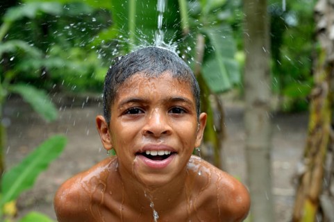Brazilian boy holding his head in a stream of water and laughing