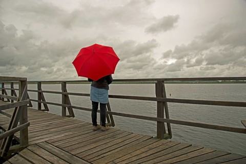 Woman holding a red umbrella on a wharf on Federsee lake