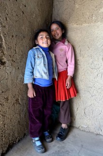 Two girls standing inside a mud-walled hut