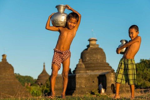 Smiling boys carrying water in front of a pagoda or a temple