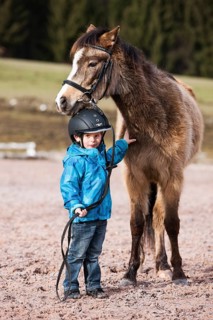 Young child wearing a riding helmet standing beside a pony