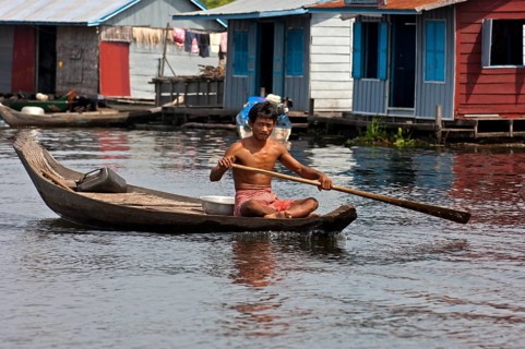 Man paddling a boat near a floating village on Tonle Sap Lake