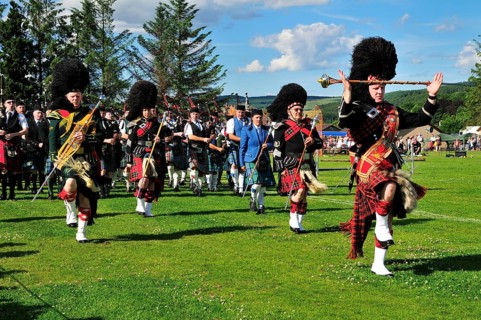 Several pipe majors leading a pipe band on the sports ground at the Highland Games