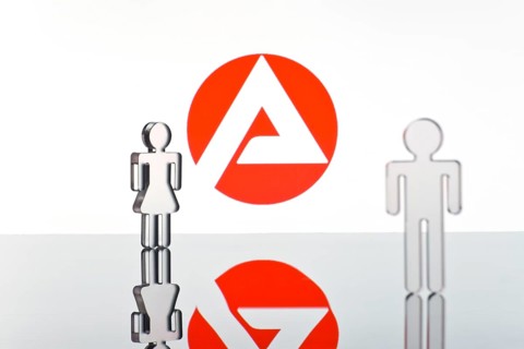 Two figures standing in front of the logo of the German employment agency