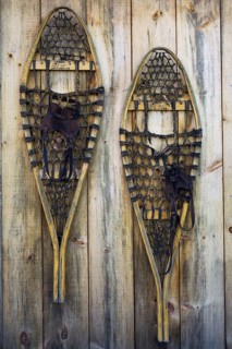 A pair of old wooden snowshoes hanging on the pine board wall of a storage shed