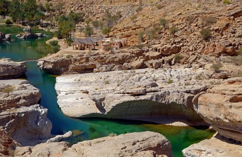 A pool filled with green water surrounded by the rocks of the desert