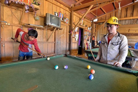 Two Cambodian youths playing pool billiards in a simple wooden hut