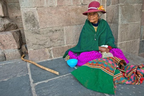 An elderly woman in traditional dress of the Quechua Indians sitting on the floor in front of an Inca wall