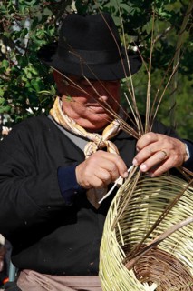 Elderly man in traditional costume making a basket at a traditional handicraft fair