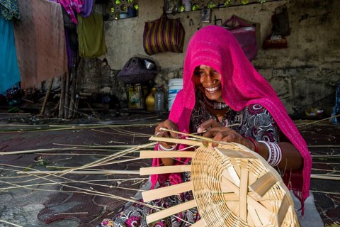 Woman covered in a pink veil is braiding a basket on the pavement
