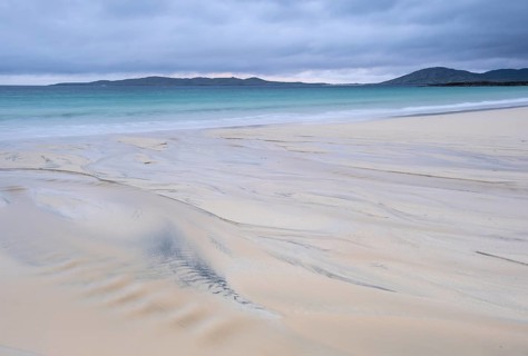 Water flows into the sea at low tide via a sandy beach