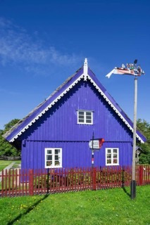 Curonian flag in front of a traditional wooden house