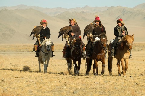 Four Kazakh eagle hunters on their horses on the way to the Eagle Festival in Sagsai