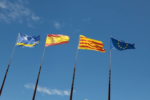 Flags of Spanish regions on flagpoles against blue sky