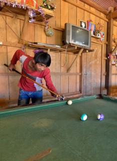Cambodian youth playing pool billiards in a simple wooden hut