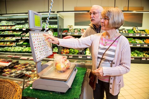 Senior couple weighing fruit at the self-service scales while shopping in the fruit and vegetables department of a supermarket