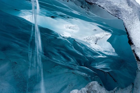 View into a blue-green ice cave with condensation water draining off