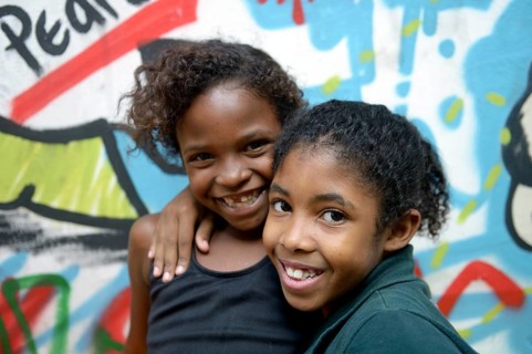 Two smiling girls embracing each other in front of a graffiti-sprayed wall