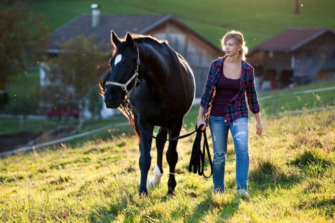 A young woman and a black Hanoverian horse walking on a mountain meadow