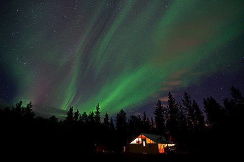 Curtains of northern polar lights and iluminated cabin