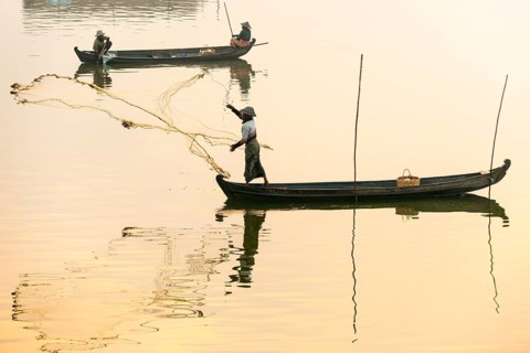 Fisherman in a boat tossing out a net