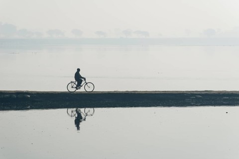 A cyclist crossing the Yamuna river on a dam in the morning haze