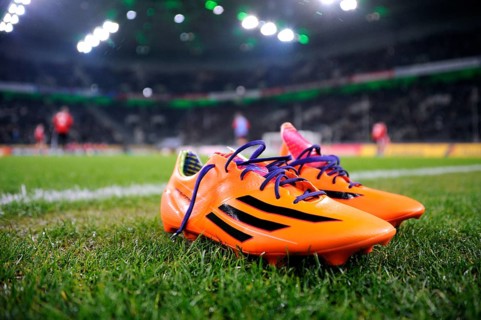 Orange-coloured Adidas football boots on the edge of the pitch