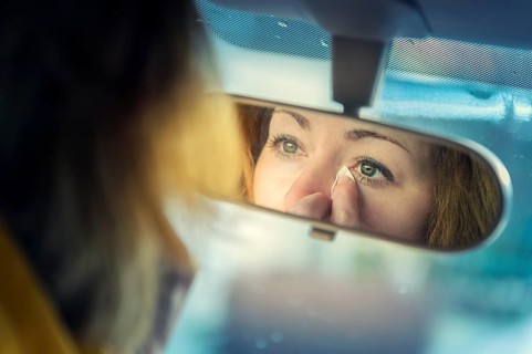 Young woman looking at herself in a rear-view mirror whilst dabbing away tears