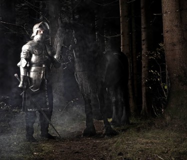 Knight wearing armour standing beside his horse in the woods