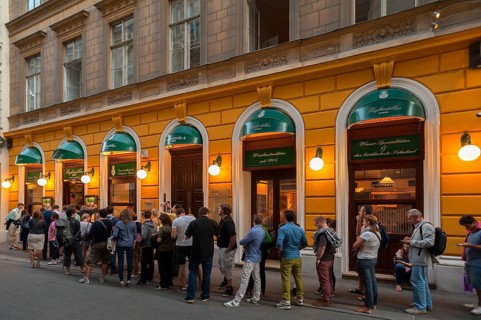 Tourists wait in long queues in front of the famous Schnitzel restaurant Figlmuller