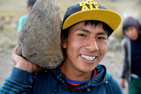 Young man carrying a heavy stone to secure the shores of an artificial lake for irrigation