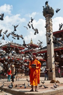 Buddhist monk with a begging bowl standing in front of Hindu temples