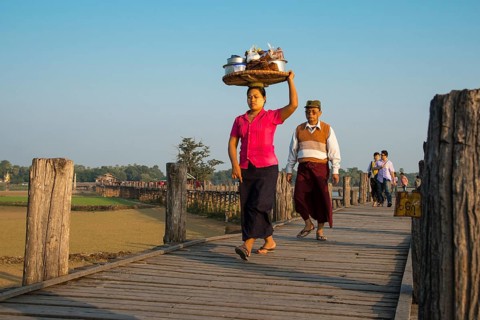 Woman with tanaka on her face carrying food on her head on a teak bridge