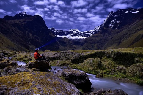 Mountaineer sitting at a mountain stream with the peaks of El Altar or Kapak Urku