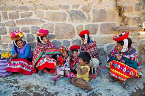 Women and children in traditional dress of the Quechua Indians sitting on the floor in front of a wall