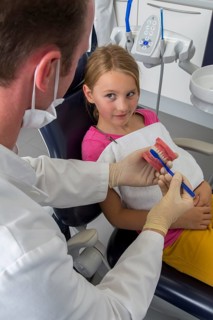 Dentist showing a girl the proper use of a toothbrush