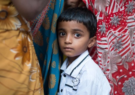 Shy Indian boy hiding between women