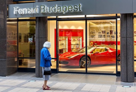 Elderly woman standing in front of the shop window of a Ferrari dealer