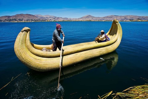 Two local people rowing a traditional boat made of totora reeds on Lake Titicaca