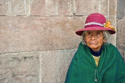 Portrait of an elderly woman in traditional dress of the Quechua Indians sitting on the floor in front of an Inca wall