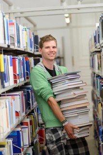 Student carrying a stack of books in the Departmental Library of the University of Hohenheim