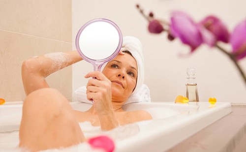 Woman taking a bath and looking at her face with a mirror