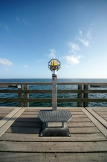 Coin-operated binoculars on a pier in front of the blue sea and blue sky