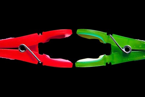 A red clothes-peg and a green clothes-peg are attacking each other