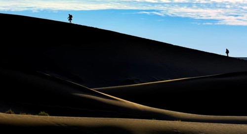 Silhouettes of people climbing a dune