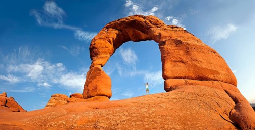 Woman standing under Delicate Arch natural stone arch